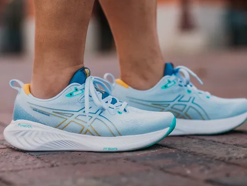 A woman stands on a brick walkway in the new ASICS Cumulus 25.