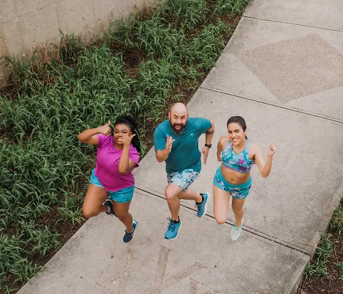 Two women and a man in running clothes smile and jump in the air