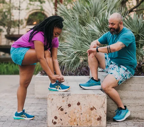 A woman and man lace up their shoes to prepare for a run
