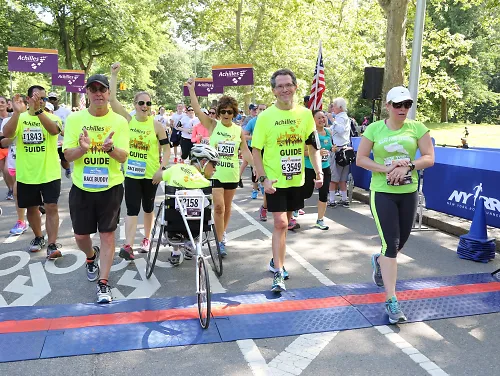 An Achilles athlete crosses a race finish line surrounded by friends and volunteers
