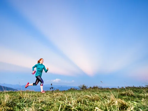 A woman running by herself on a trail through a meadow