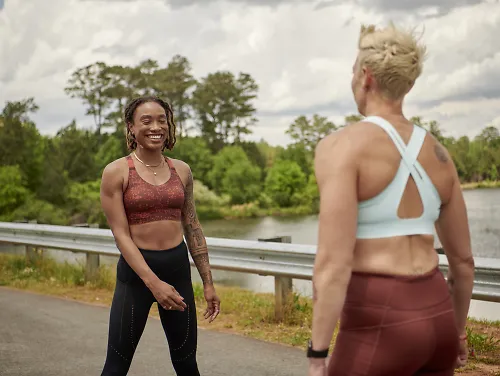 Two woman wearing Brooks Dare Run Bras laugh together before a run.