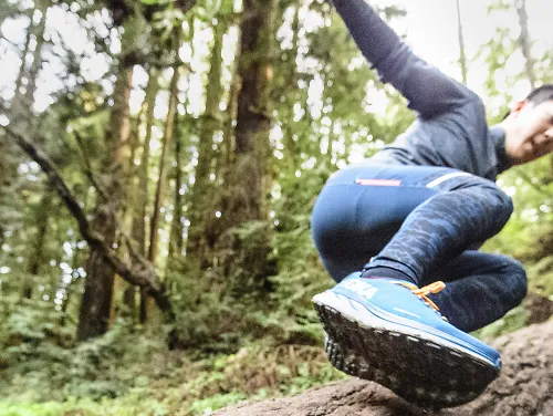 A runner jumps over a log in the woods