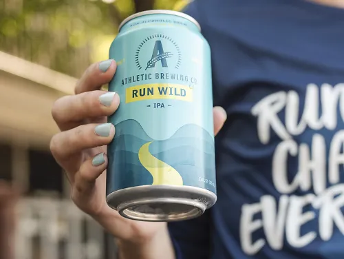 A woman holds a chilled can of Run Wild IPA by Athletic Brewing