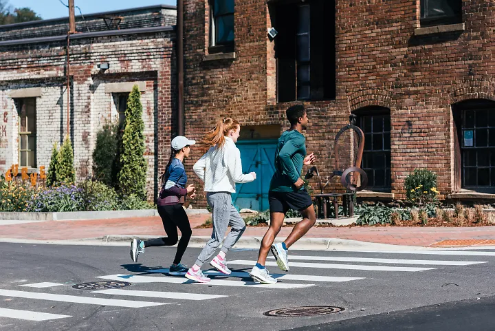 A man and two women run together in front of a brick building