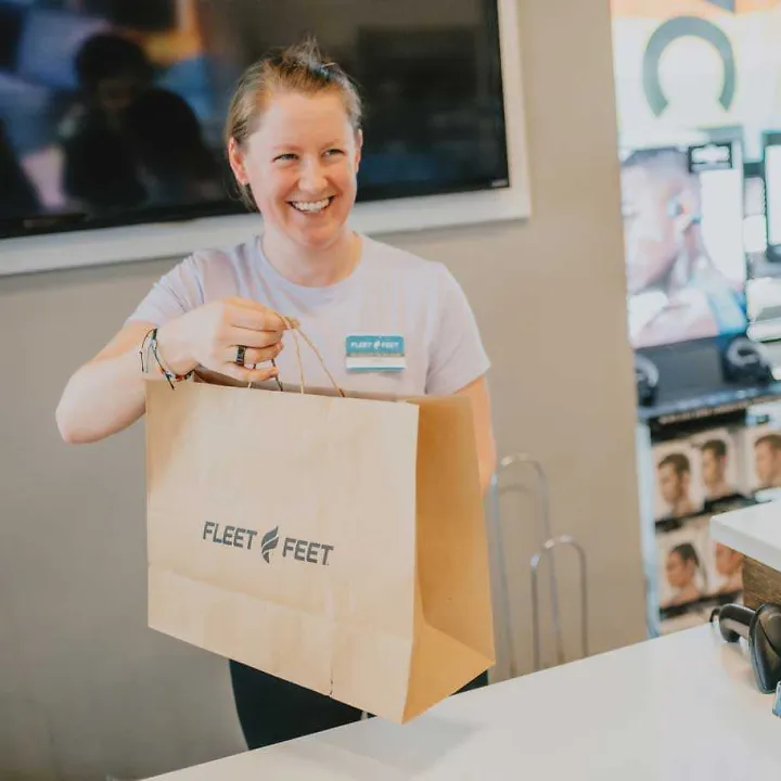 woman passing a Fleet Feet bag across a counter