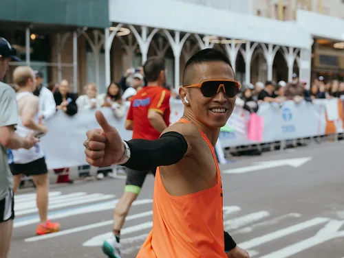 A man grins and flashes a thumbs up to the camera while running the New York City Marathon. 