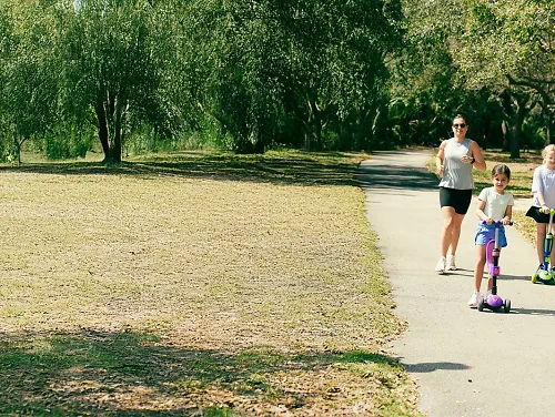 Mother running alongside two daughters on scooters
