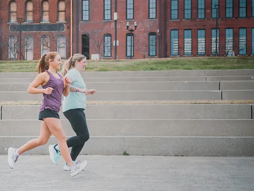Two women running alongside staircase and buildings