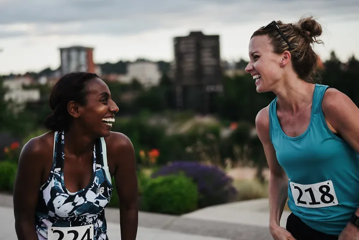 Two female runners wearing race bibs laughing alongside one another