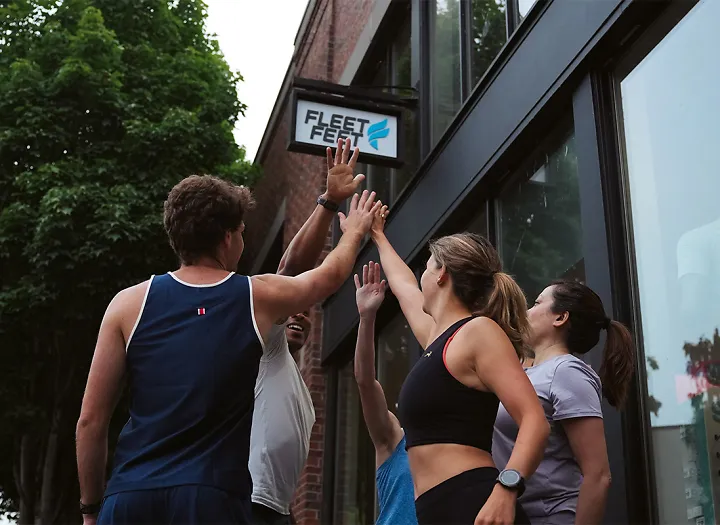 runners high-fiving in front of fleet feet store