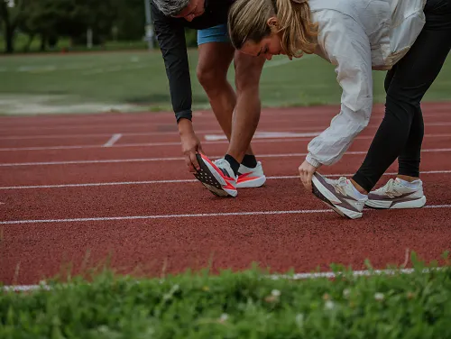 2 people bending over stretching on a track outside