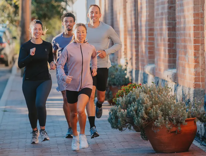 a group of people running outside on brick pavement next to a brick building with greenery plants outside the building