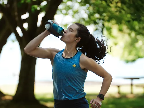 A woman drinks from a handheld bottle during a run. 