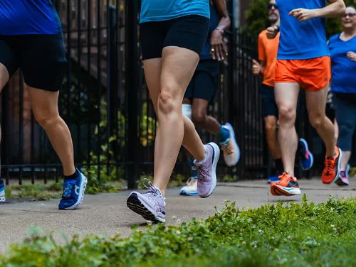 Close up of running groups shoes as they run down sidewalk along a fence