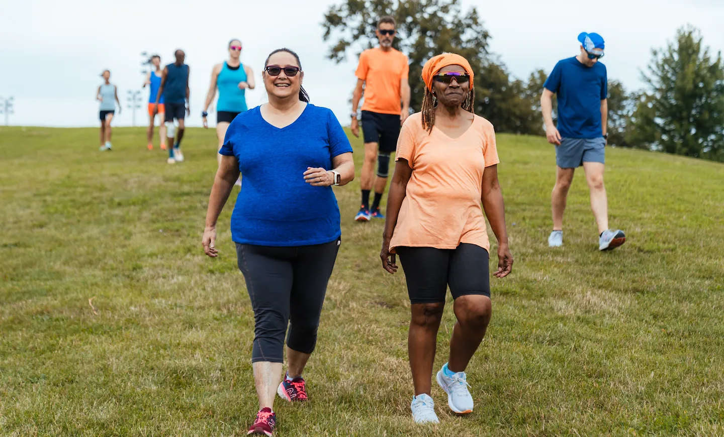 A group of Fleet Feet runners smiles as they walk together down a hill on a beautiful summer day