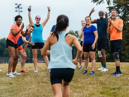 A woman runs up a hill toward her smiling, cheering teammates waiting at the top