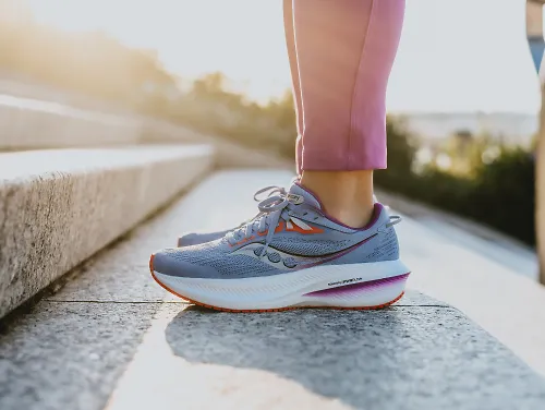 A woman stands on the steps in a pair of Saucony Triumph 21. 