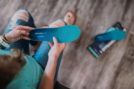 A woman's hands are shown holding a blue pair of Superfeet Dynamic Run insoles
