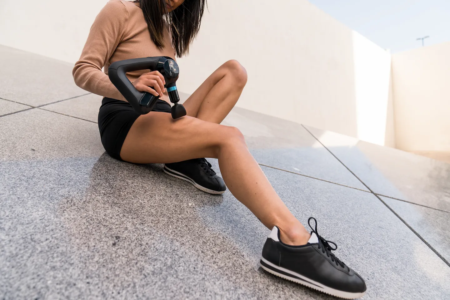 A woman uses the Theragun Elite massage gun on her legs. 