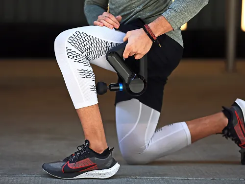 A runner uses the Therabody Theragun Elite massage gun on their calf.