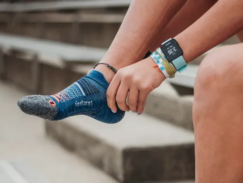 A runner sitting on bleachers puts on a pair of Feetures running socks