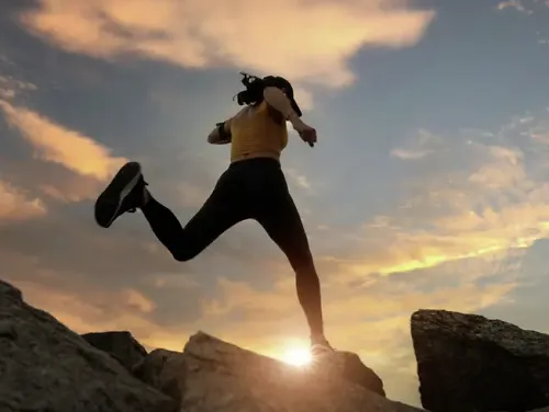 A runner jumps across rocks in front of a setting sun