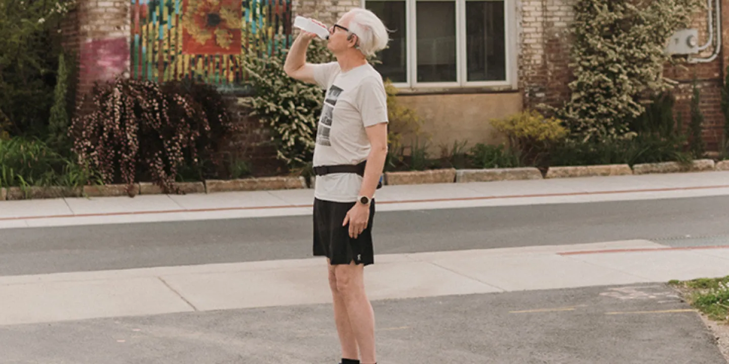 An older man pulled his water bottle from his hydration belt and is drinking it.