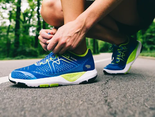 A woman kneeling to tie a pair of Karhu Ikoni running shoes