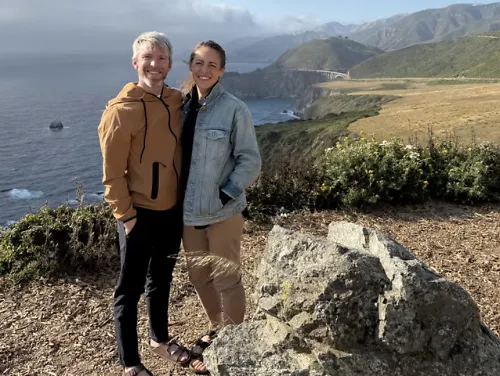 Jenny Simpson and Jason Simpson stand on a cliff with ocean in the background