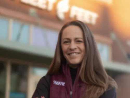 Jenny Simpson stands, smiling, in front of a Fleet Feet store