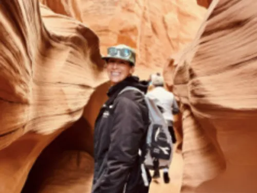 A woman smiles while standing in a canyon, wearing a backpack and outdoor gear