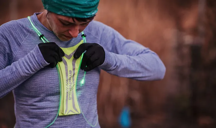 A woman tightens a lighted running vest around her chest before a run