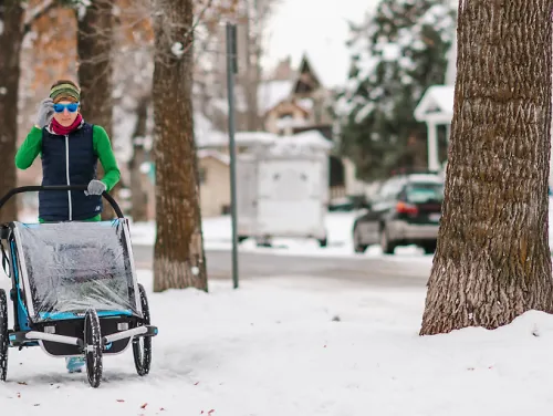 A runner pushes a stroller through snow in winter